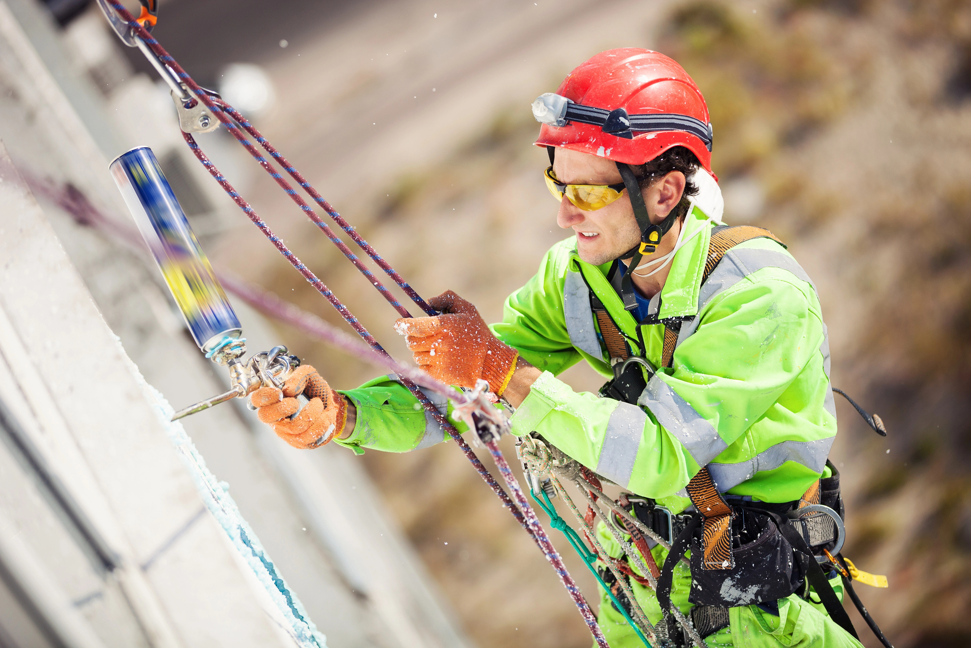 Male construction worker on the job with a helmet, fall Protection harness, high visibility yellow jacket.